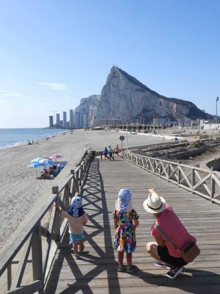Rodzina z dziećmi spacerująca po drewnianym pomoście przy plaży w okolicy Gibraltaru