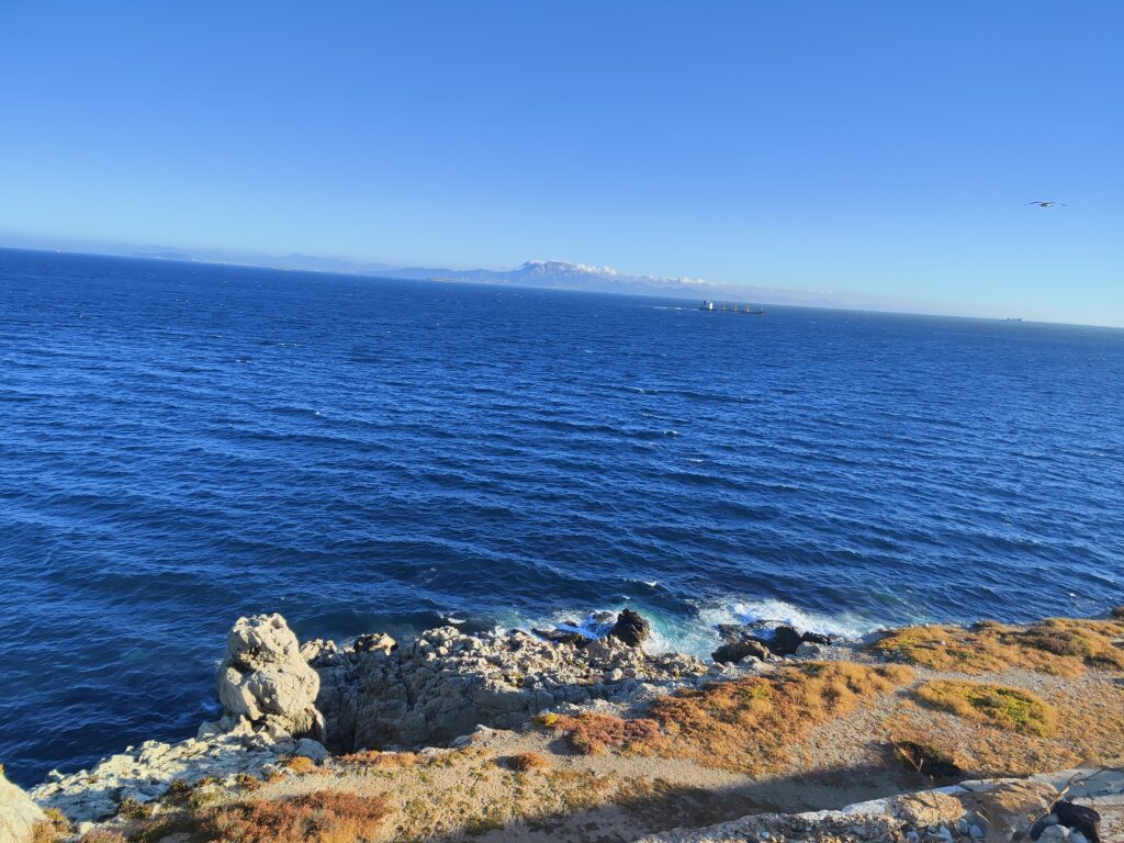 Widok na Cieśninę Gibraltarską - morze, płynący statek, w oddali góra w Afryce, fale rozbijające się o skaliste wybrzeże